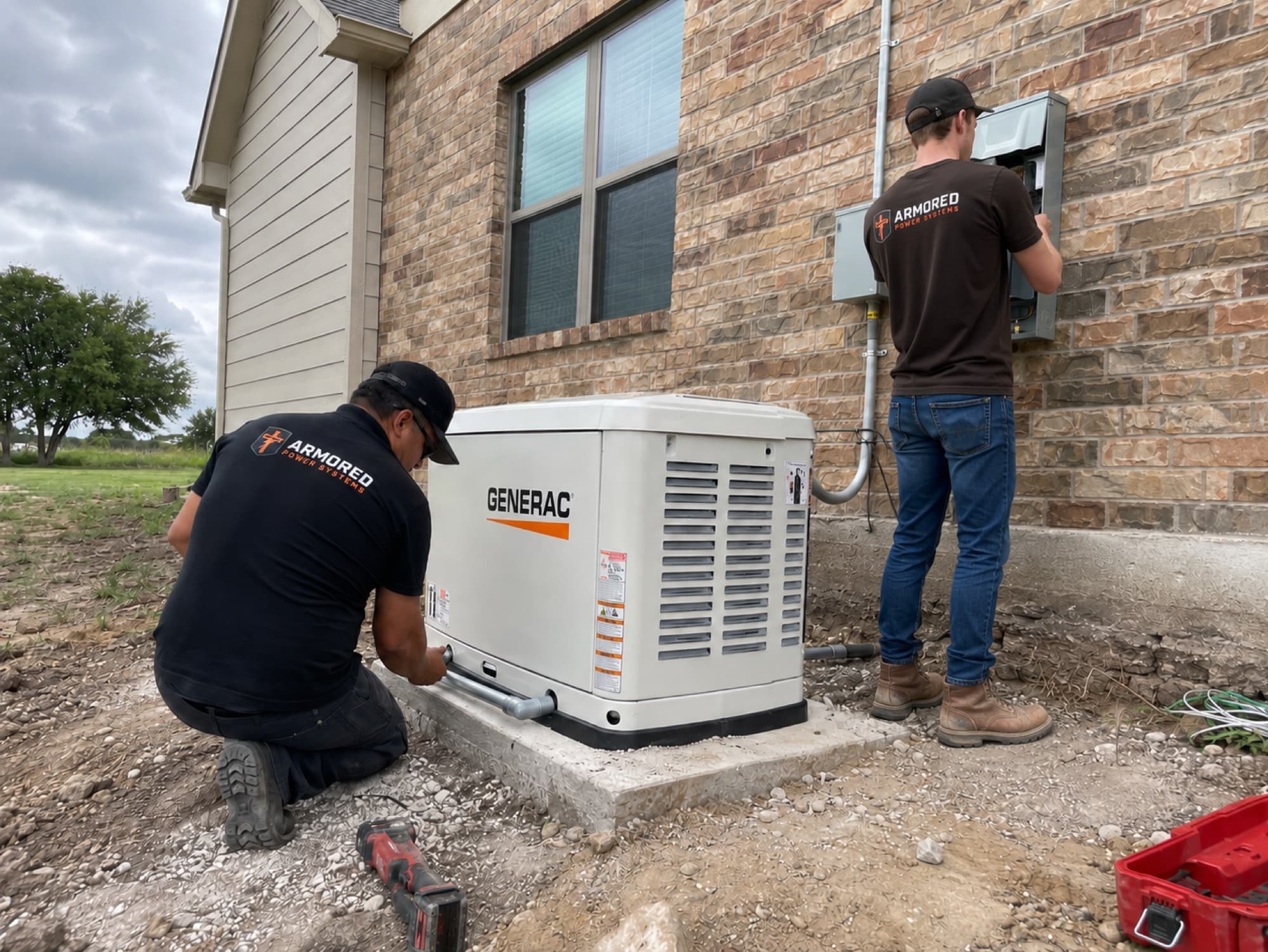 Armored Power Systems technicians installing a Generac standby generator on a concrete pad beside a brick home on a rural lot.