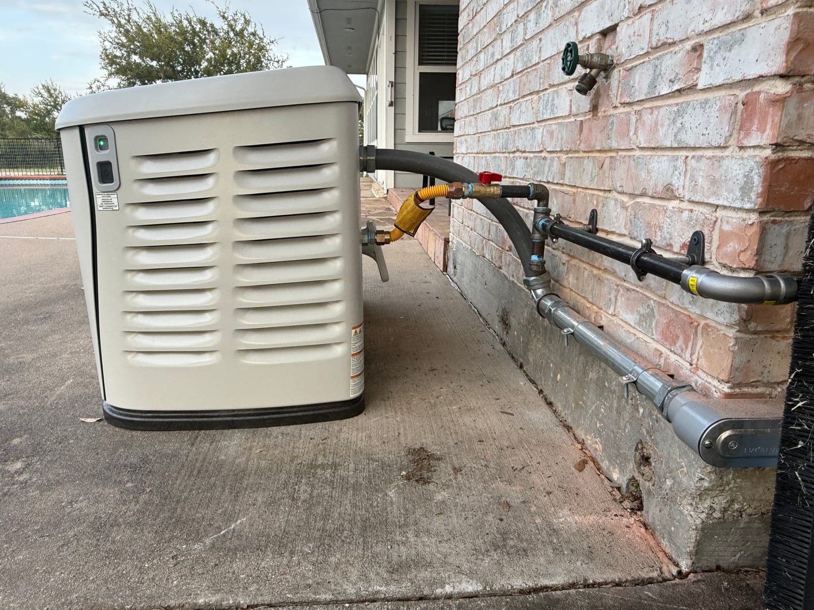 A finished Generac home standby generator on its pad beside a brick wall, with the gas line and conduit run in along the wall.