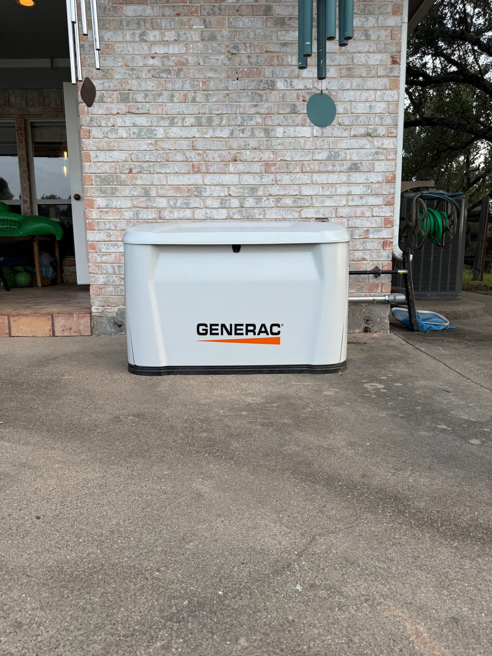 A Generac home standby generator installed on a concrete pad against a brick exterior wall.