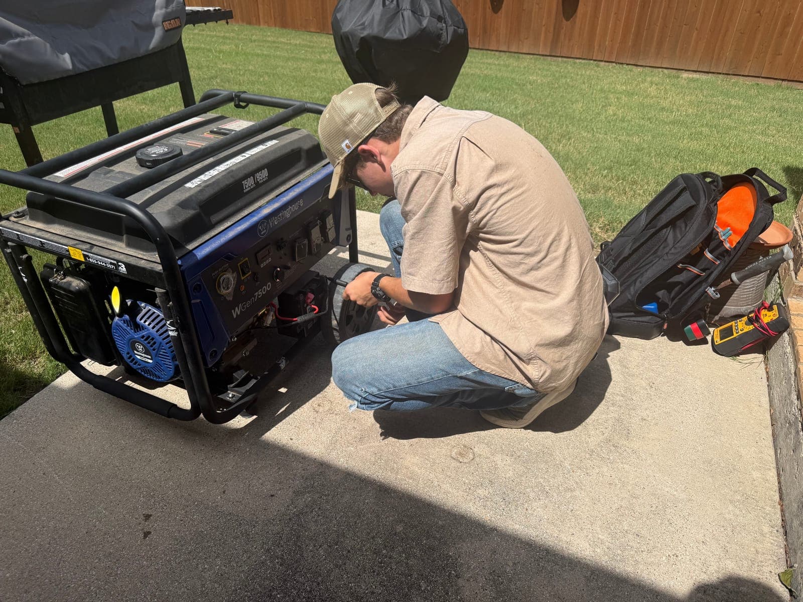 An Armored Power Systems technician commissioning a generator on site, kneeling at the unit with a tool bag open beside him.