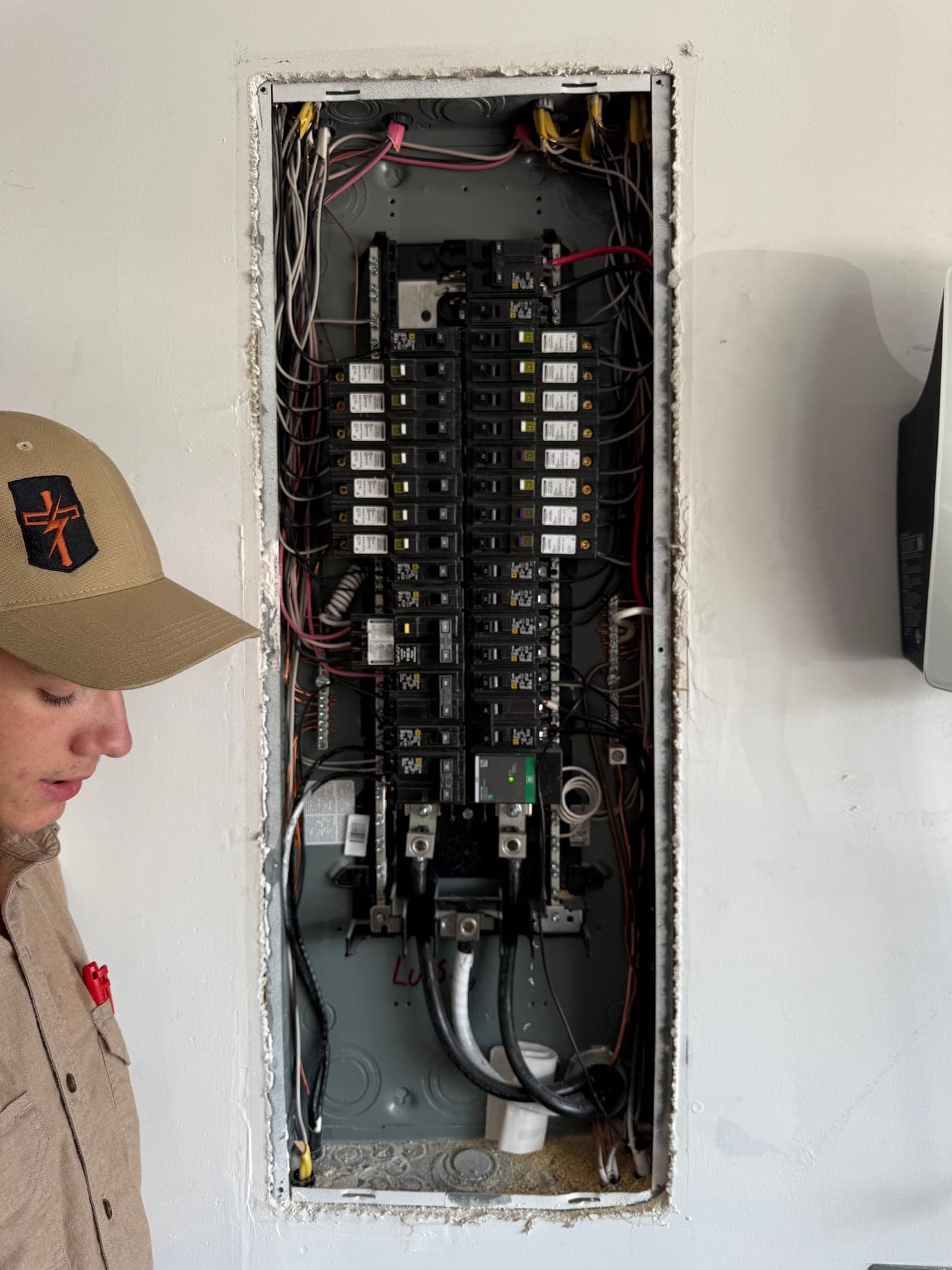 An Armored Power Systems technician working at an open residential load centre recessed into an interior wall.