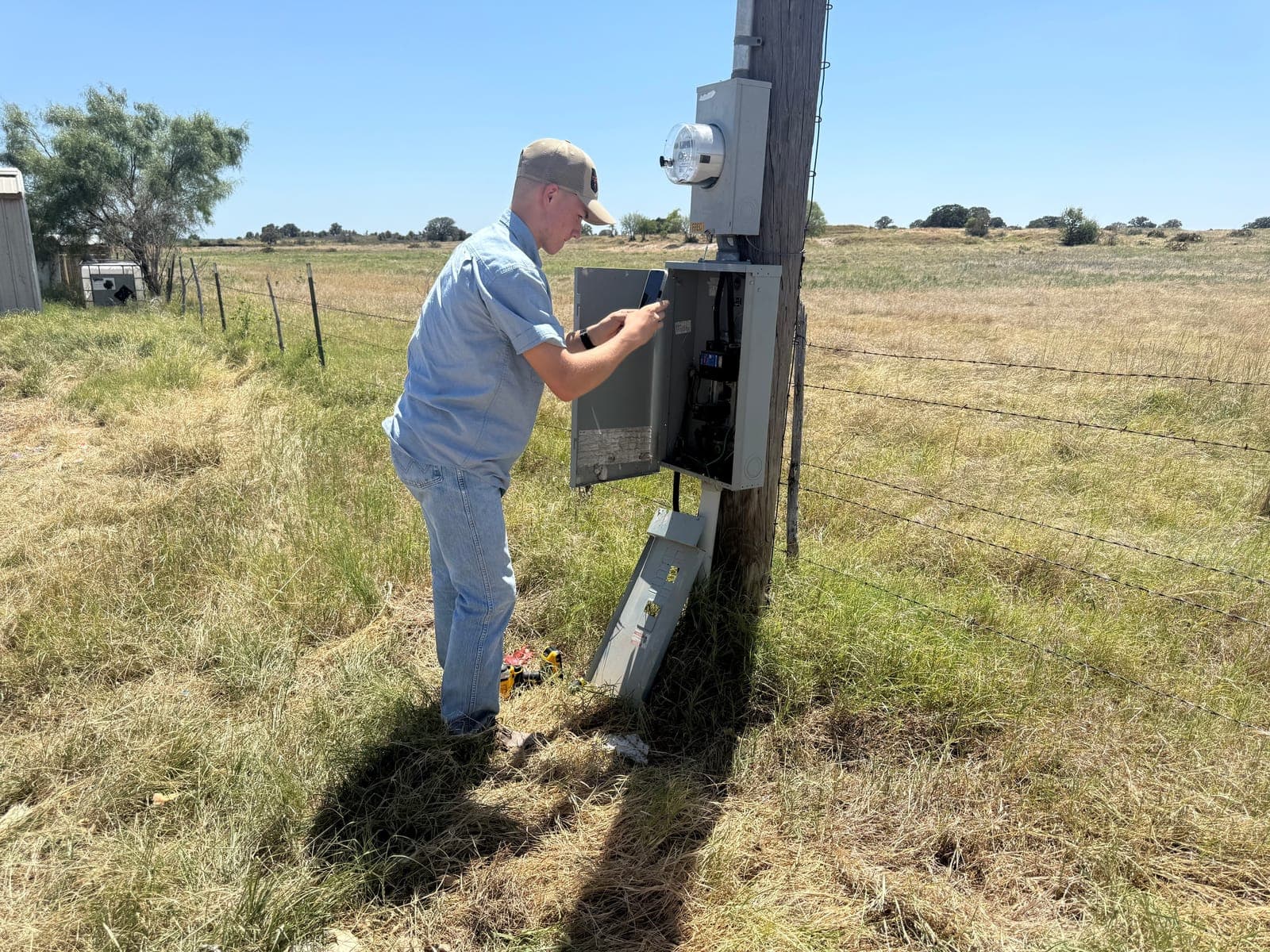 An Armored Power Systems technician working inside a meter and disconnect enclosure on a pole at the edge of a pasture.