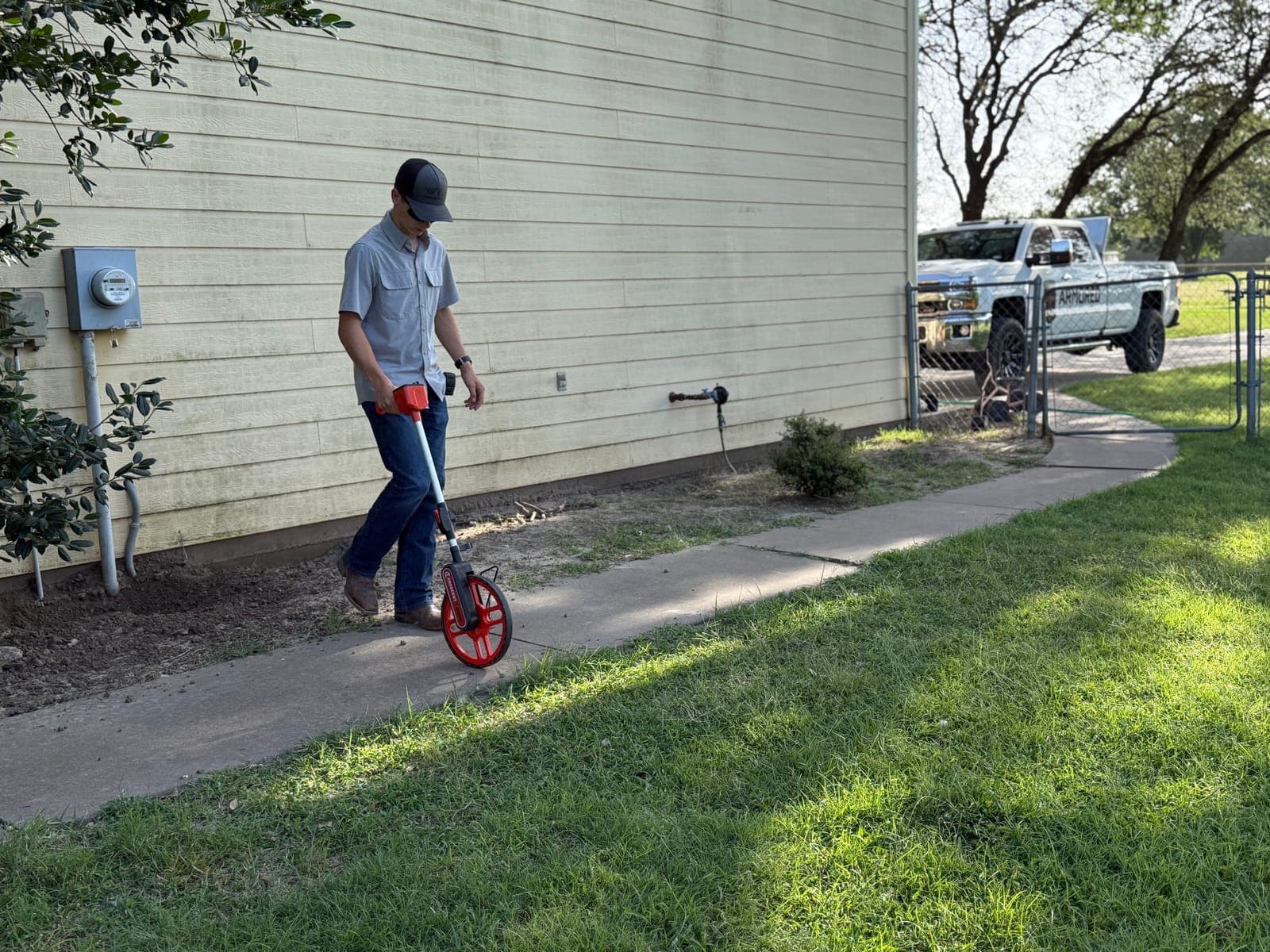 An Armored Power Systems technician walking the side of a property during a site assessment, service truck parked at the kerb.