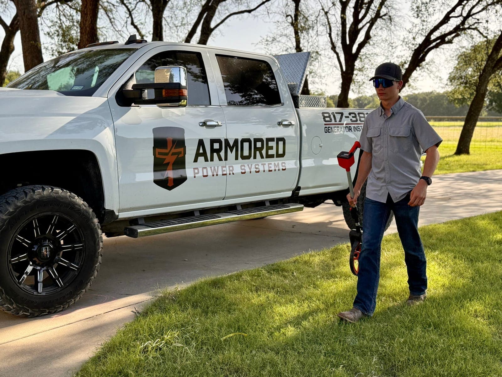 An Armored Power Systems technician beside a branded company truck on a rural Texas driveway.
